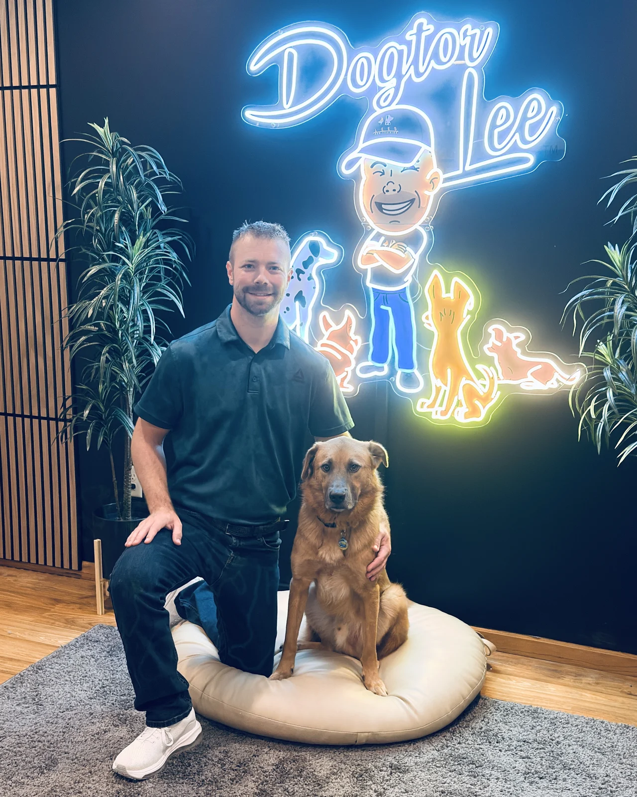 Lee Seibold kneeling with his dog Shooter in front of the Dogtor Lee neon sign at his Huntington, IN training facility
