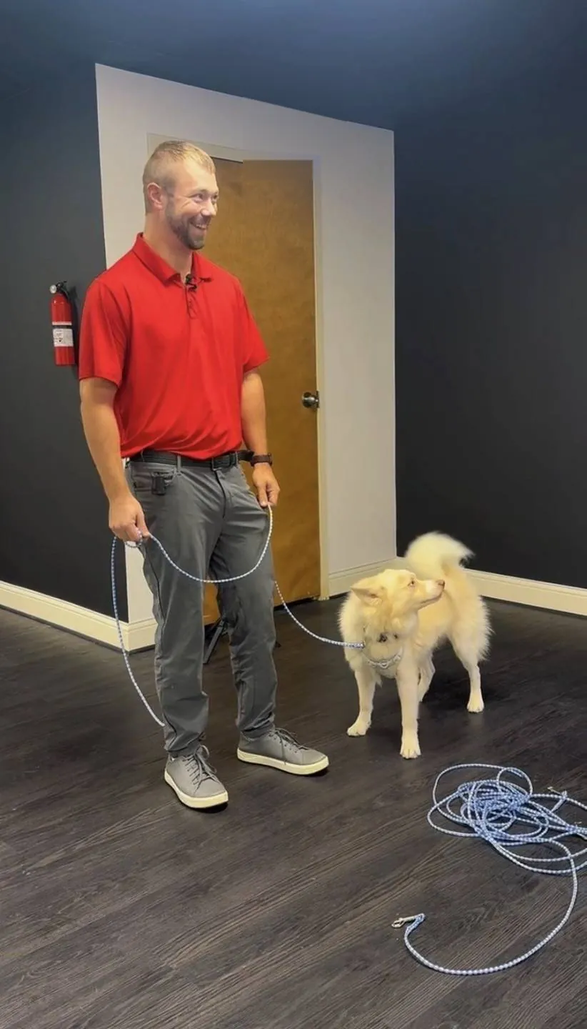 Lee Seibold in a red polo with a calm, off-leash dog in his training room